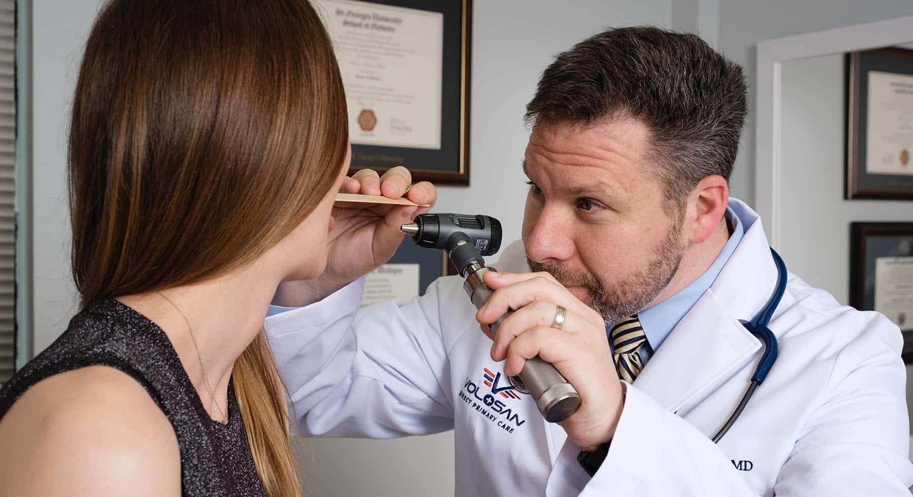 Dr Fine examining the throat of a female patient in an exam room.
