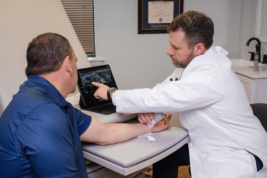 Dr Fine reviewing on-screen test results with a male patient in an exam room.
