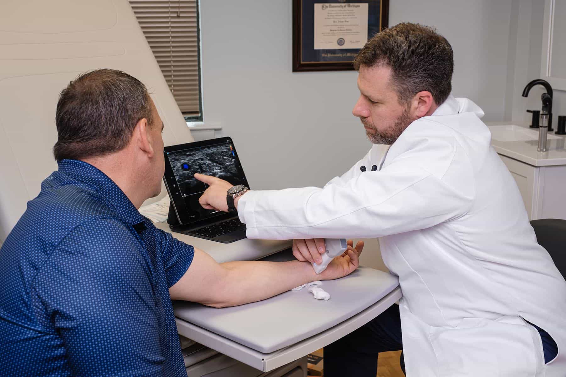 Dr Fine reviewing on-screen test results with a male patient in an exam room.