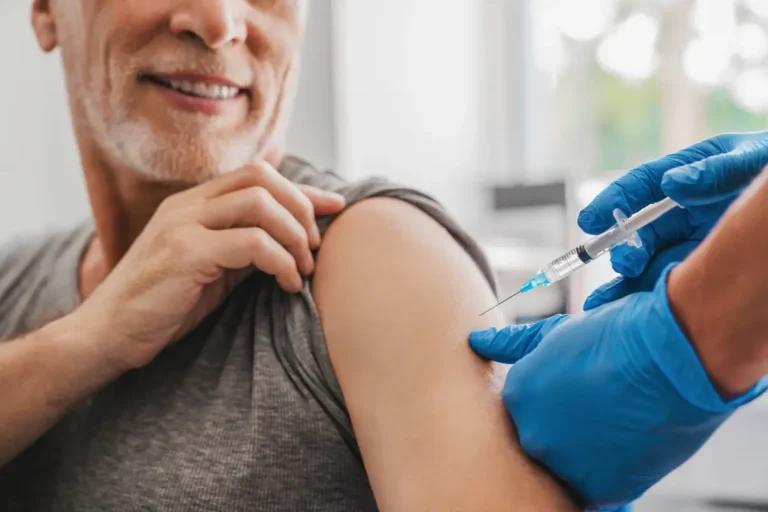 Doctor injecting medication into the arm of a smiling male patient.